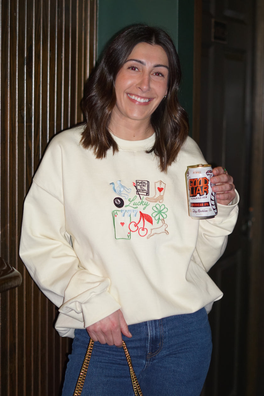 Woman wearing an ivory crewneck sweatshirt embroidered with colorful lucky-inspired icons.