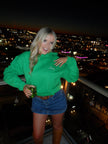 Woman wearing a bright green hoodie with white embroidered “Lucky” lettering, paired with a denim mini skirt at night.