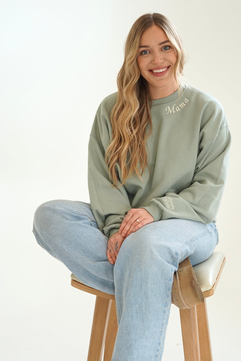Model wearing a sage green personalized Mama embroidered crewneck sweatshirt with light wash jeans.