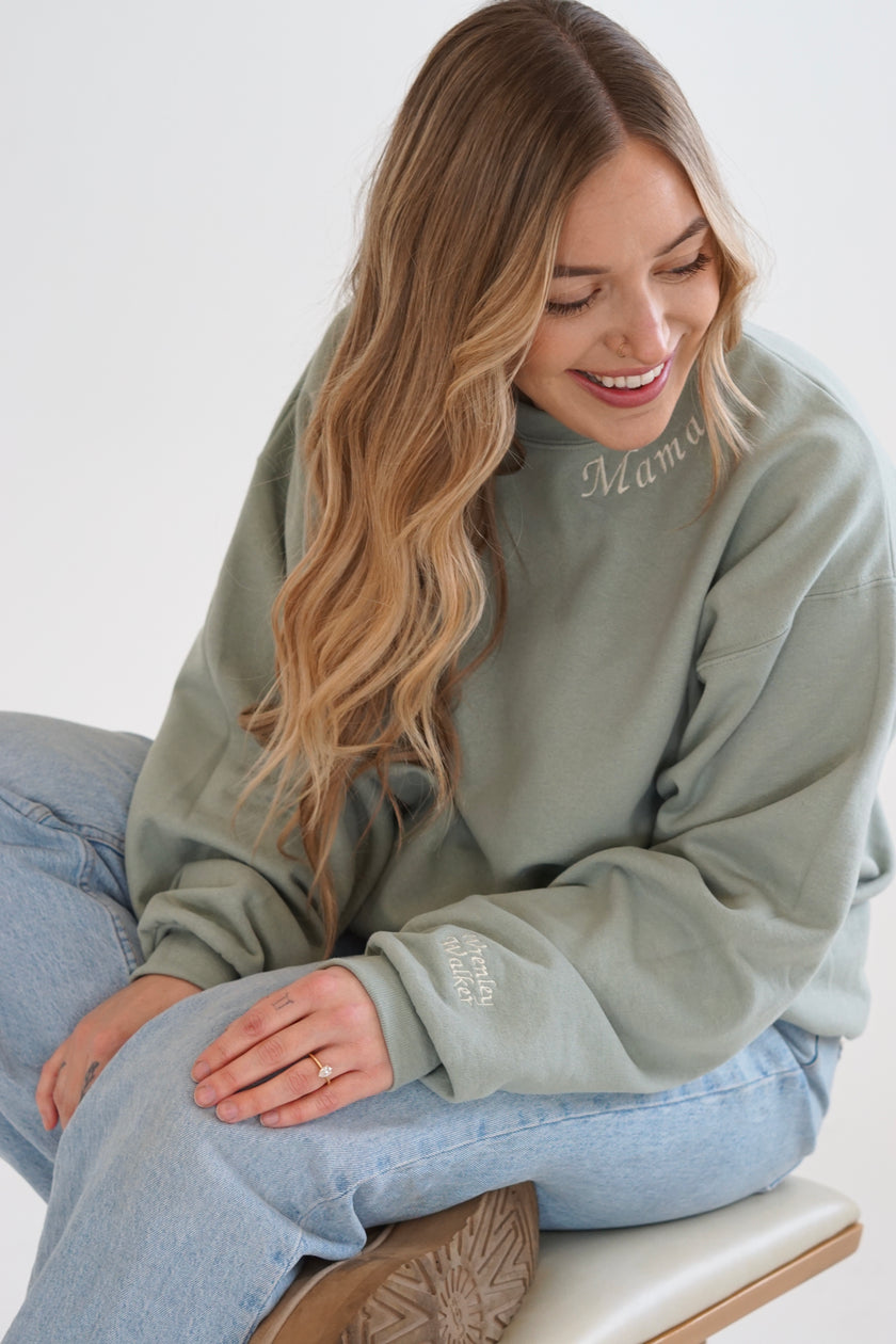 Close-up of a sage green personalized Mama embroidered crewneck sweatshirt featuring custom neckline and sleeve embroidery.