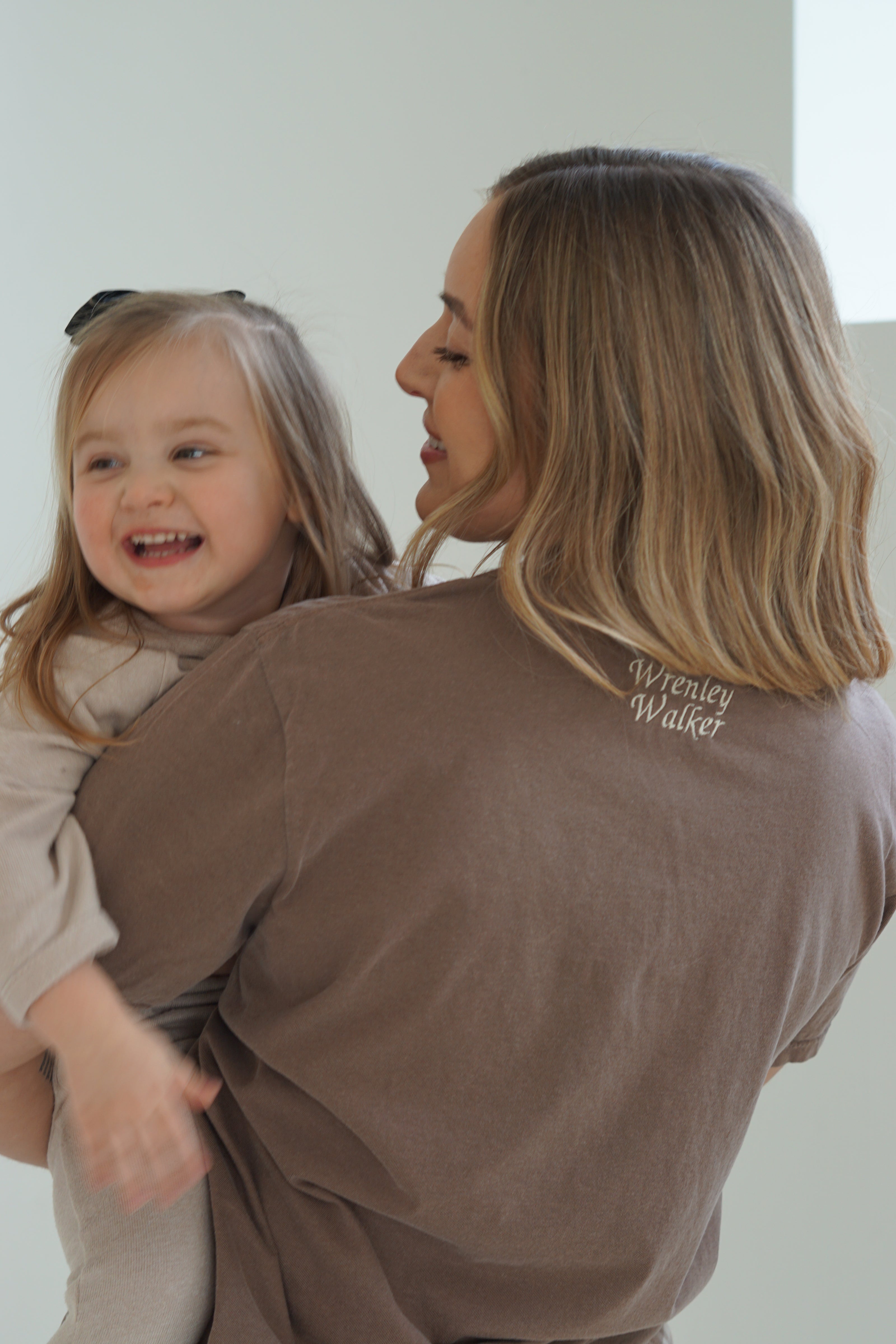 Back view of a personalized Mama embroidered T-shirt featuring custom name embroidery while a mom holds her young daughter.