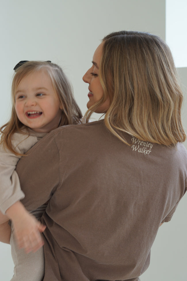 Back view of a personalized Mama embroidered T-shirt featuring custom name embroidery while a mom holds her young daughter.
