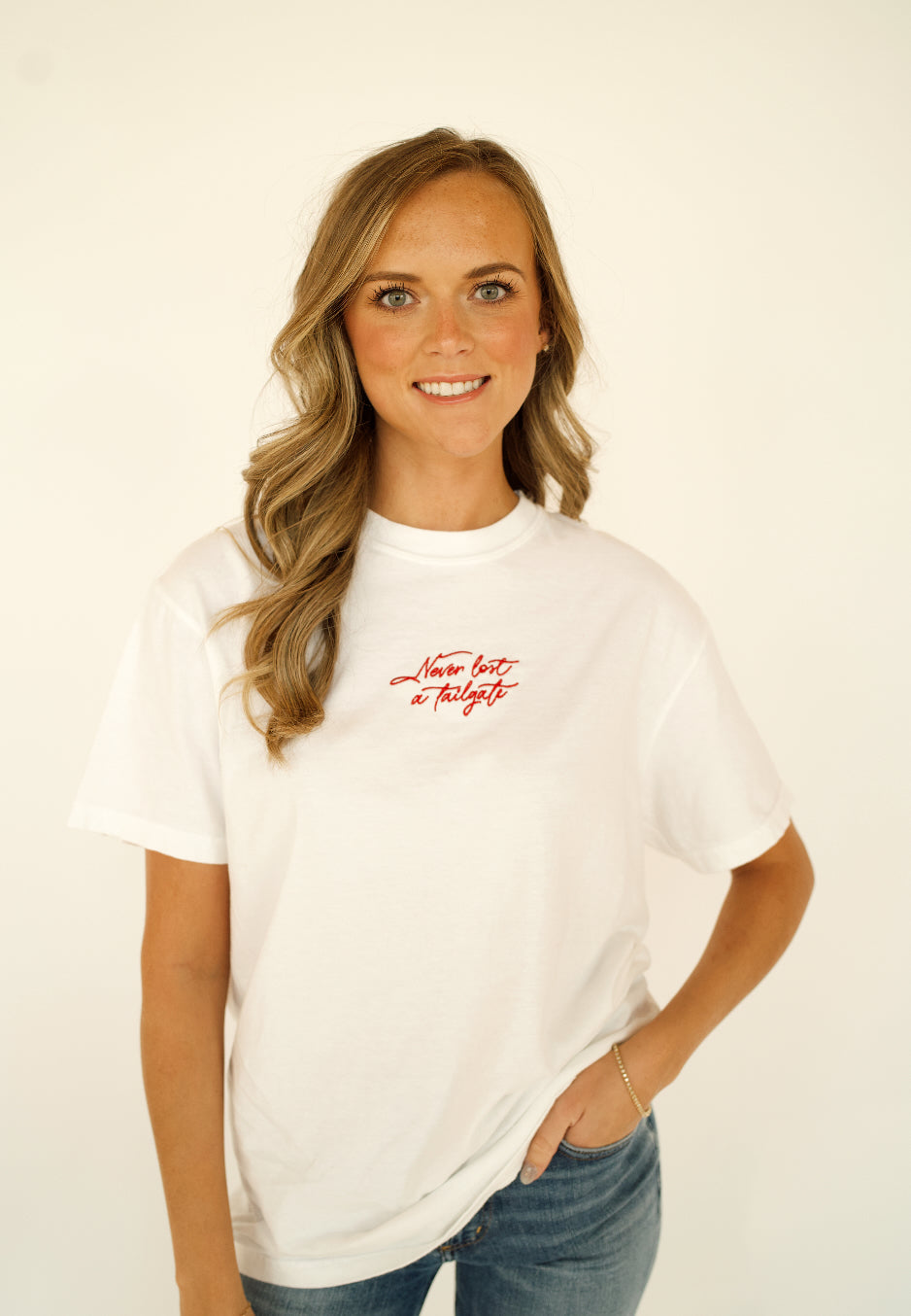 Woman wearing a white Never Lost a Tailgate embroidered, game day T-shirt.