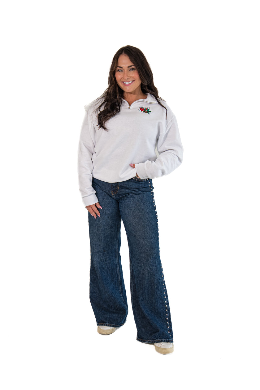 A woman modeling a white long-sleeve quarter-zip pullover with a small embroidered logo on the left chest, paired with dark blue jeans featuring decorative stitching down the outer legs, against a solid white background.
