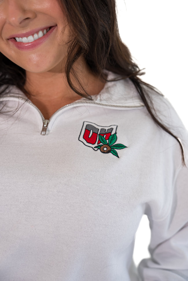 A close-up of a woman wearing a white half-zip pullover sweatshirt with a red, white, and green Ohio logo embroidered on the left chest.