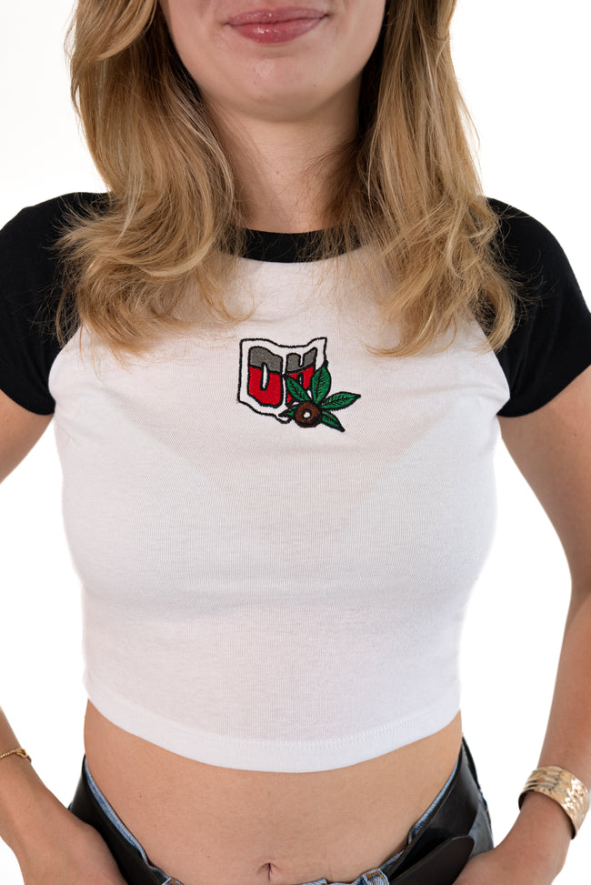 Close-up of the front of a white ribbed ringer t-shirt with black sleeves, featuring a detailed embroidered patch of the state of Ohio with a buckeye and leaves.