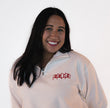 Woman wearing a white quarter zip sweatshirt with red embroidered flags, spelling 