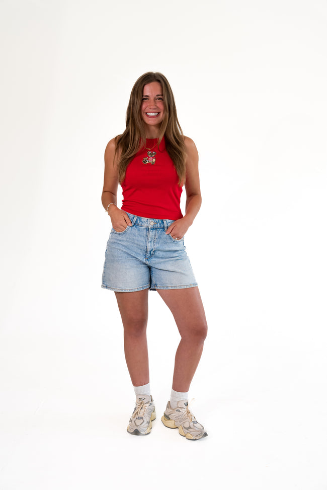 Woman wearing a bright red ribbed high-neck tank top featuring a stitched teddy bear patch on the chest, dressed in an Ohio football uniform and holding a football, paired with light-wash denim shorts.
