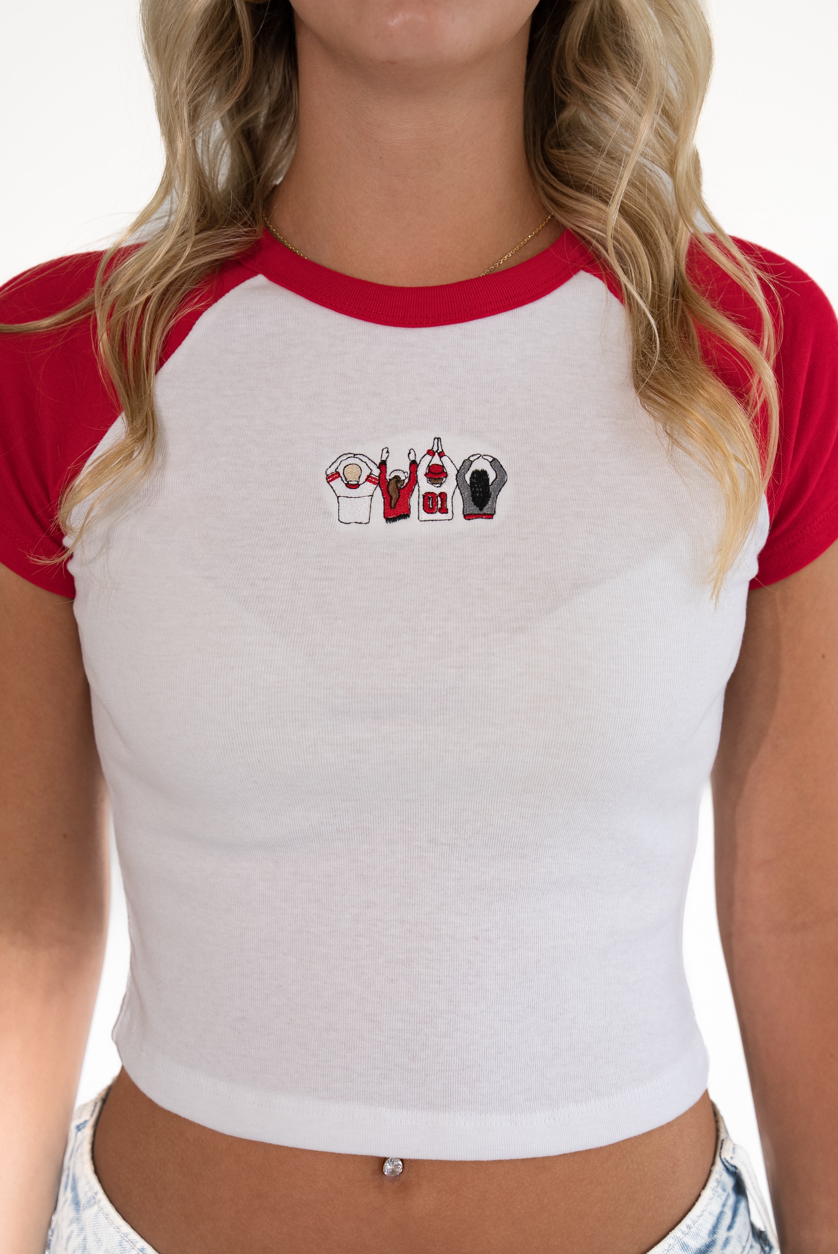 A woman wearing a white and red raglan crop top with a small graphic on the chest, shown from the neck to the hips against a plain white background.