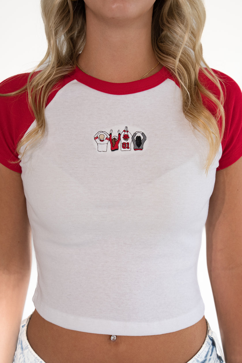 A woman wearing a white and red raglan crop top with a small graphic on the chest, shown from the neck to the hips against a plain white background.