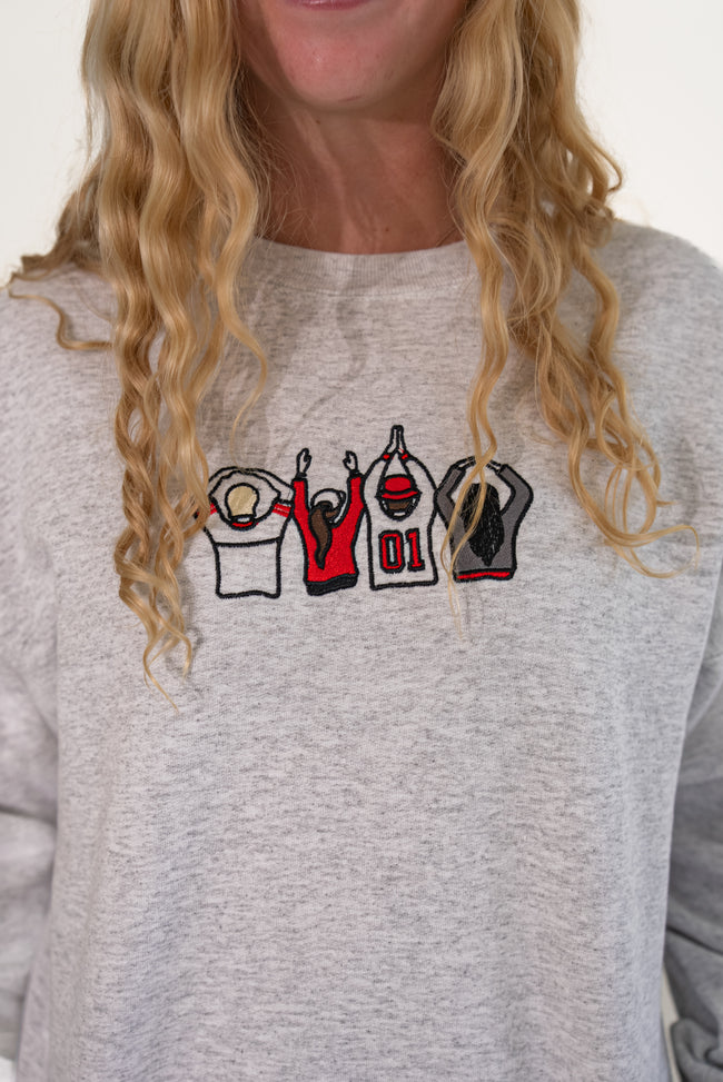 Close-up of a woman wearing a heather gray sweatshirt with an embroidered Ohio-themed graphic on the chest