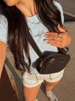 Woman wearing a light blue fitted baby tee with an embroidered airplane and “on holiday” lettering, styled with white shorts and a crossbody bag.