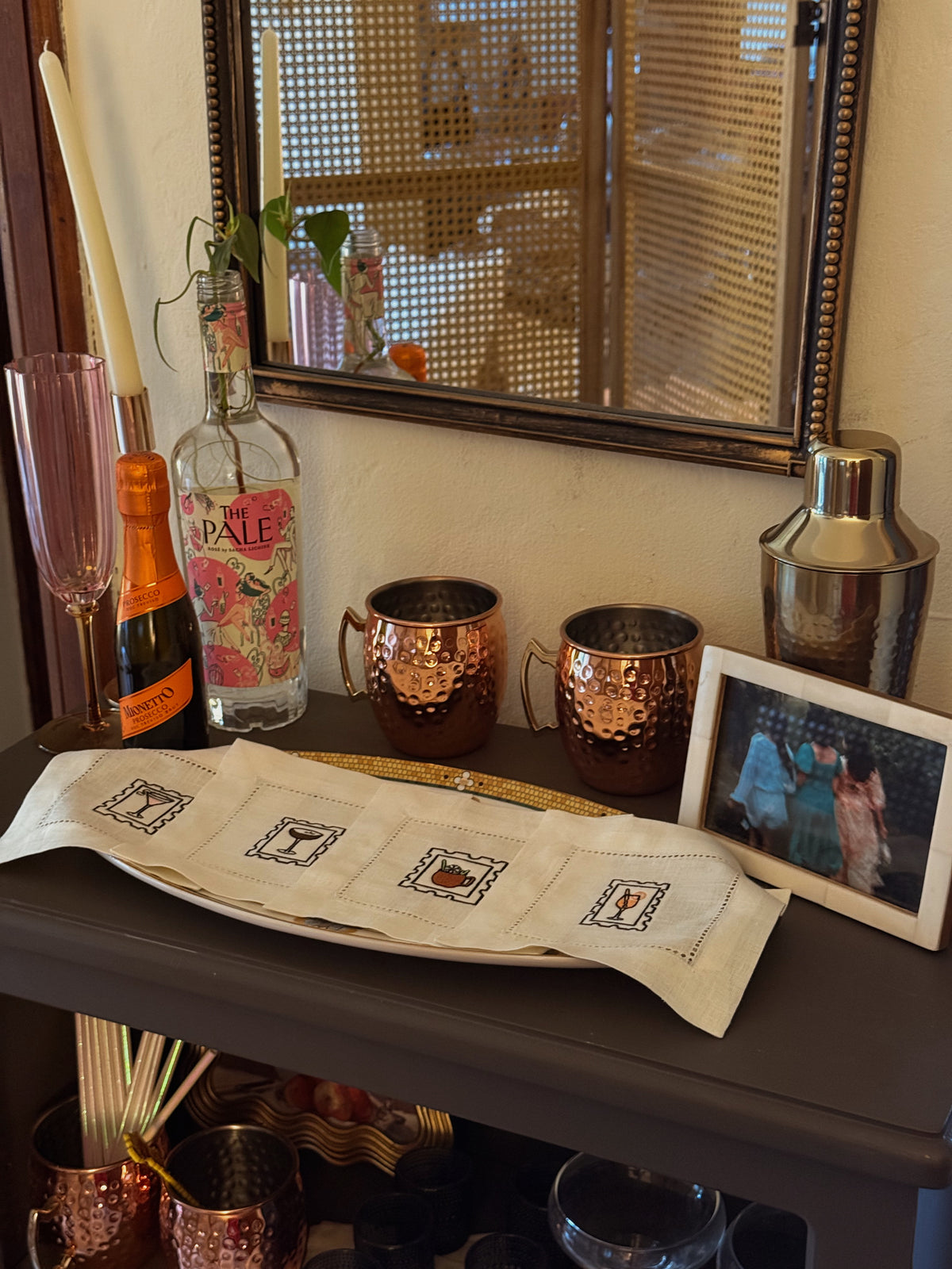 Bar setup with bottles, mugs, and a mirror reflecting a person.