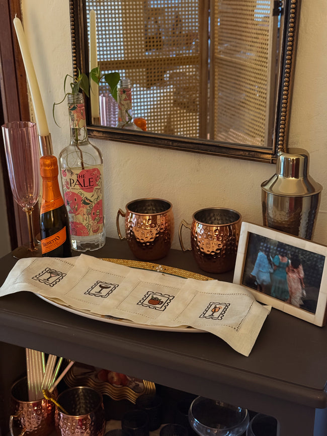 Bar setup with bottles, mugs, and a mirror reflecting a person.