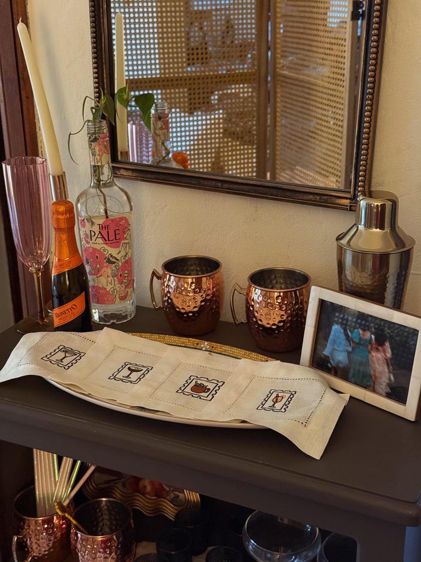 Bar setup with bottles, mugs, and a mirror reflecting a person.