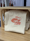 Cream baby tee or tank with coral embroidered shrimp and cocktail design on the chest.