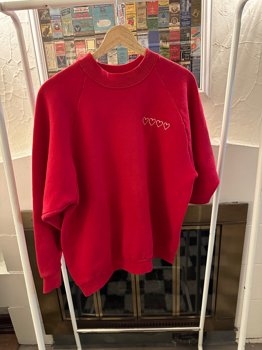 Close-up of the minimalist Valentine's embroidery stitched on the front of the red crewneck.