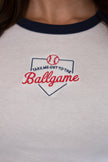 Close-up of the front of a white ringer tee with a navy collar, featuring a detailed embroidered home plate graphic with 