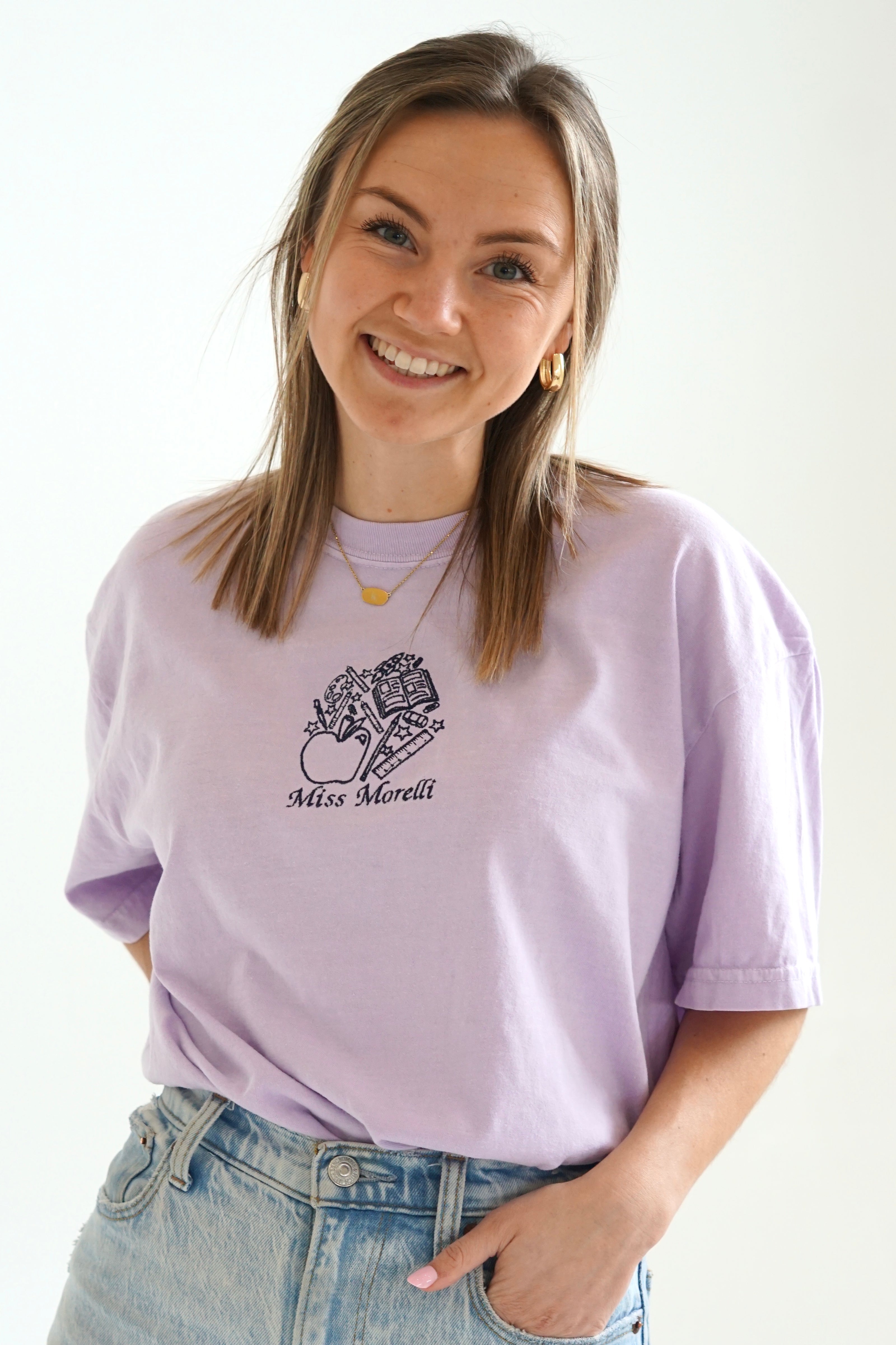 Model wearing a personalized teacher T-shirt with custom embroidered school-themed design and blue jeans.