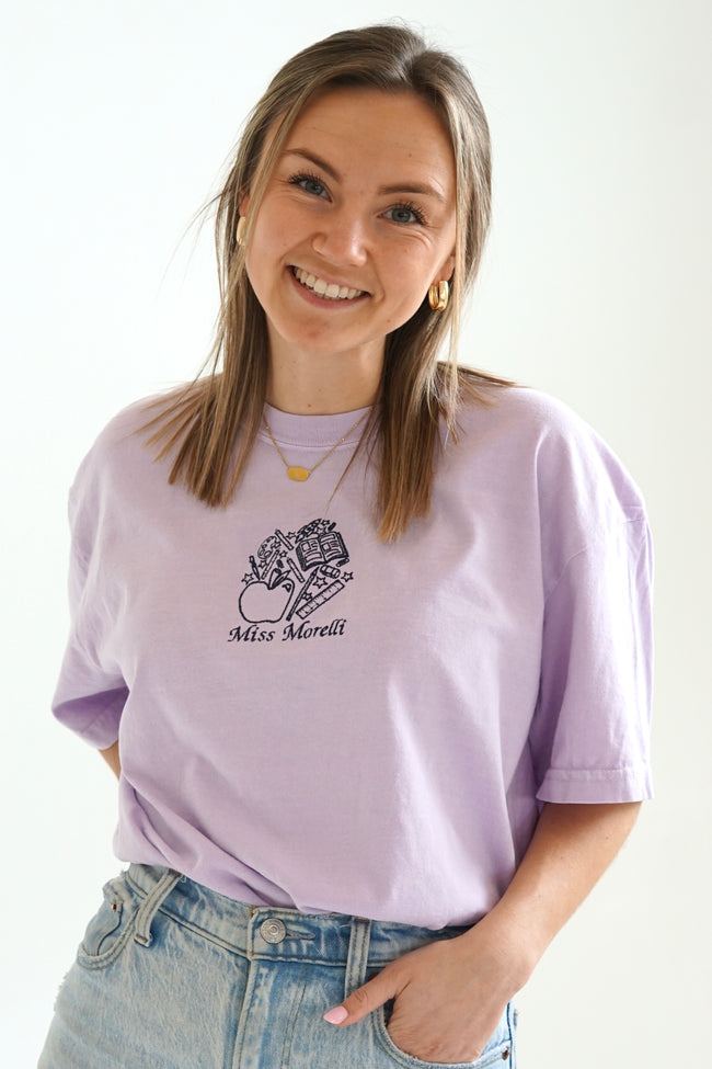 Model wearing a personalized teacher T-shirt with custom embroidered school-themed design and blue jeans.
