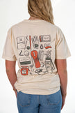 A woman viewed from behind wearing a cream-colored graphic t-shirt with a golf-themed illustration on the back, paired with blue jeans against a white studio background.