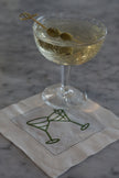 Embroidered martini cocktail napkin used as coasters beneath cocktail on a marble bar.