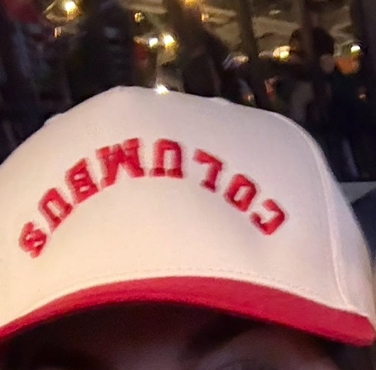 Close-up of a white trucker hat with a red brim and red embroidered 