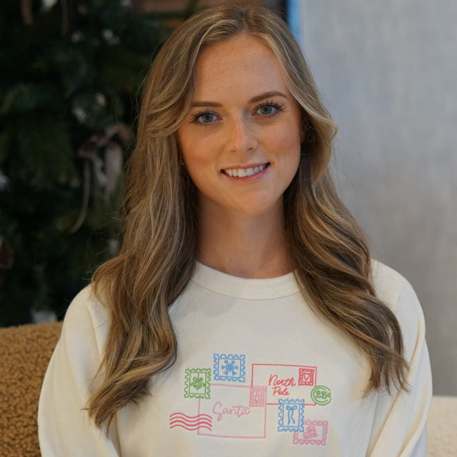 Woman wearing an ivory Letter to Santa embroidered crewneck sweatshirt featuring a festive holiday postcard design.
