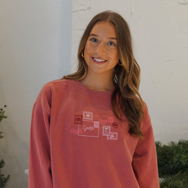 Woman wearing a red Letters to Santa graphic crewneck sweatshirt featuring a festive holiday postcard design.