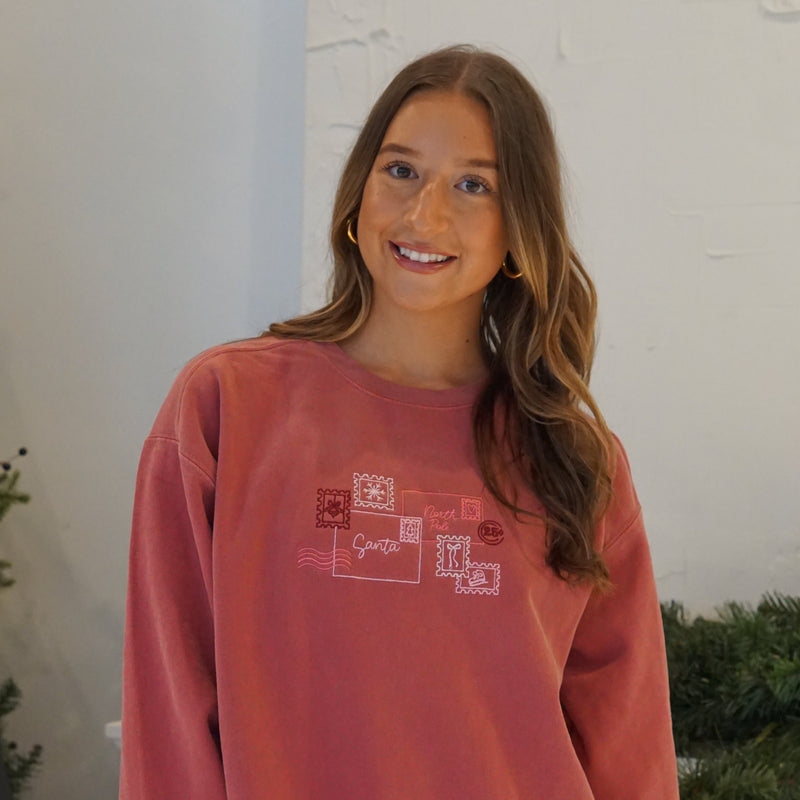 Woman wearing a red Letters to Santa graphic crewneck sweatshirt featuring a festive holiday postcard design.