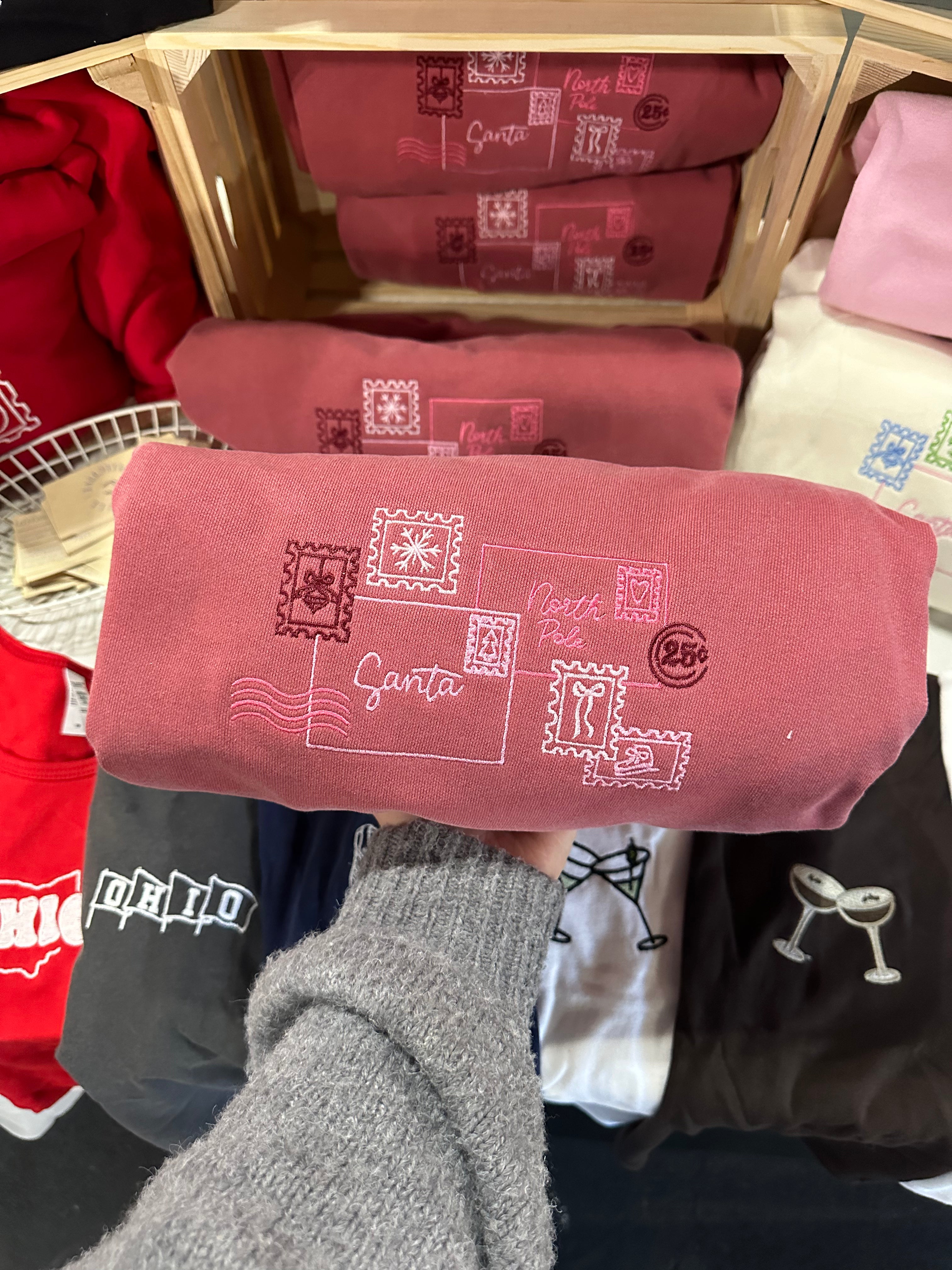 Folded red Letter to Santa crewneck sweatshirt featuring an embroidered holiday postcard design.