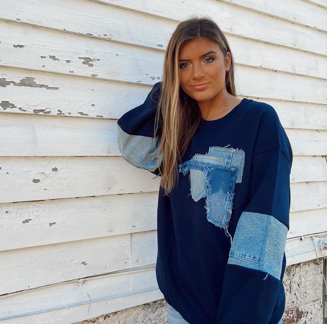 Woman wearing a navy oversized sweatshirt with distressed denim patchwork on the front and sleeves.