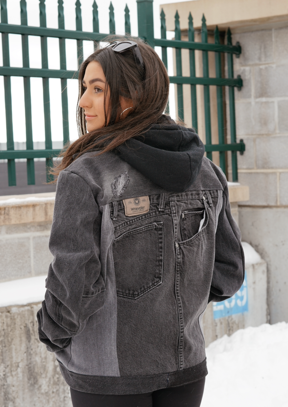 Back view of a woman wearing a black color-block denim jacket with oversized fit and contrasting denim panels.