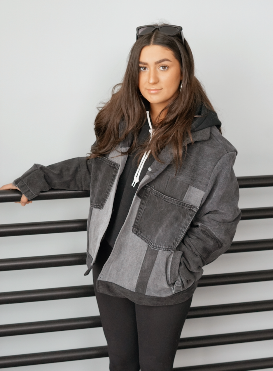 Woman wearing a black color-block denim jacket with oversized fit and front patch pockets.