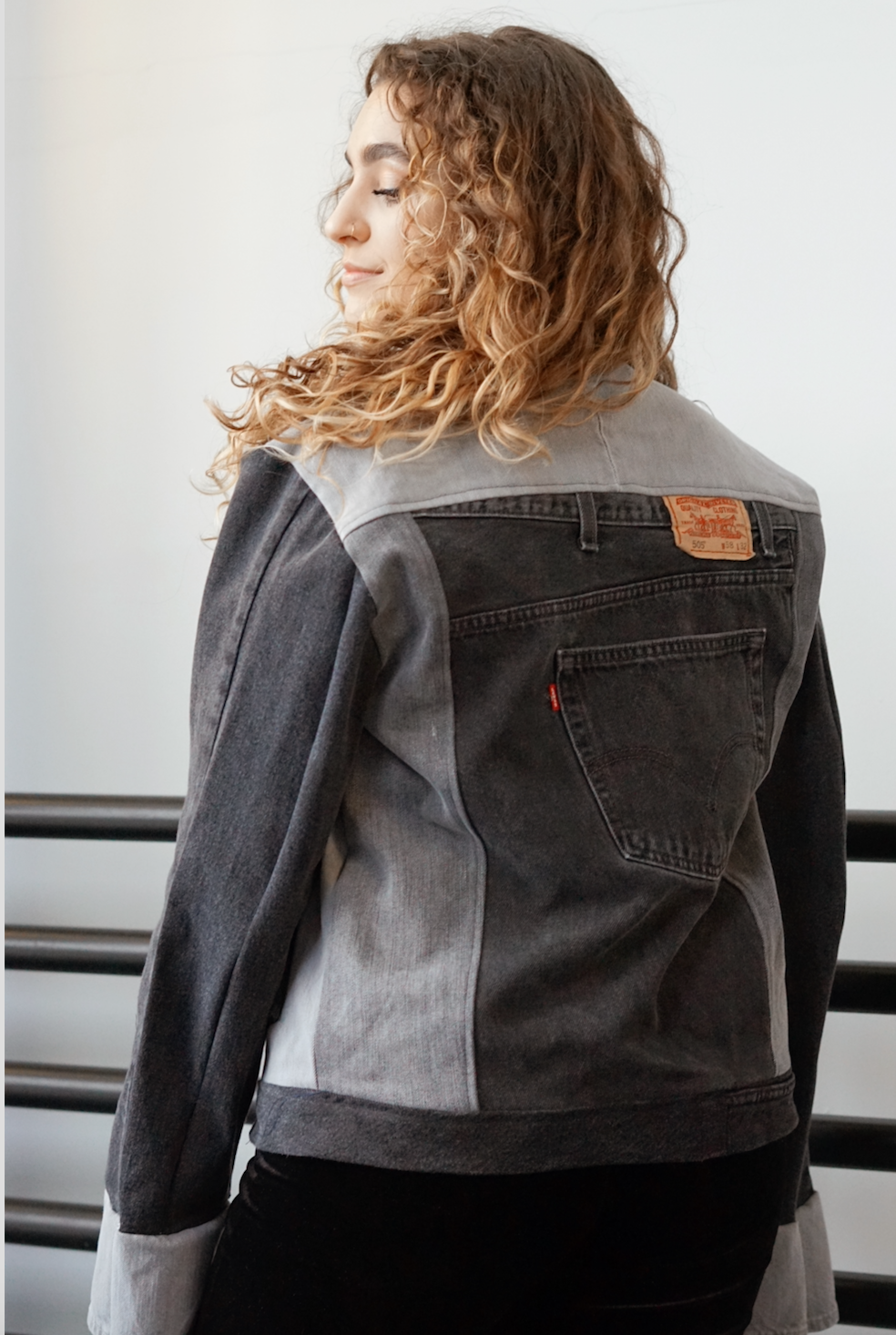 Back view of a woman wearing a black color-block denim jacket with contrasting gray denim panels.