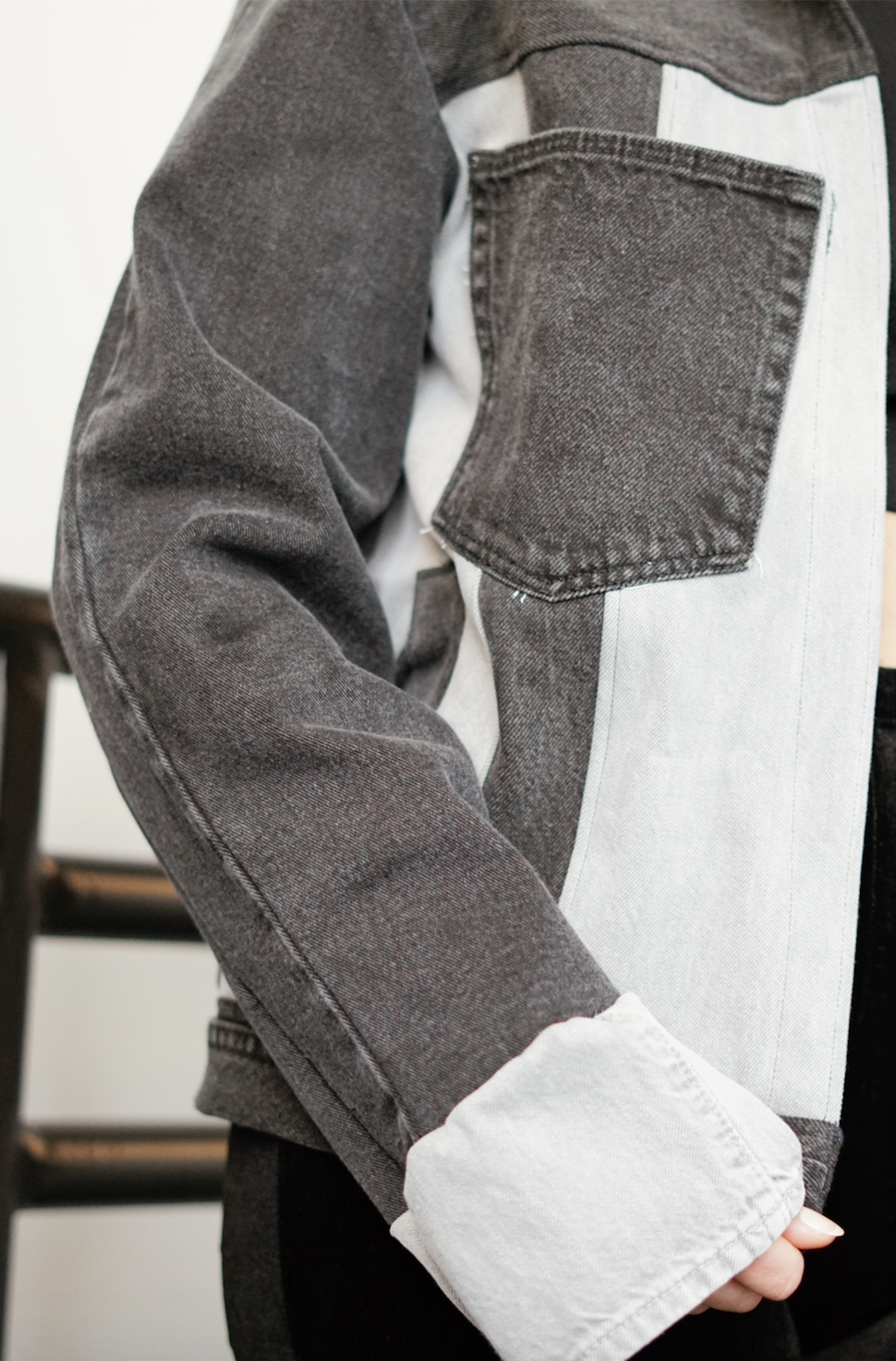 Close-up of a black color-block denim jacket with contrasting gray denim panels and front patch pocket.