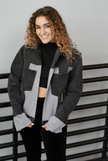 Woman wearing a black color-block denim jacket with contrasting gray denim panels and front patch pockets.