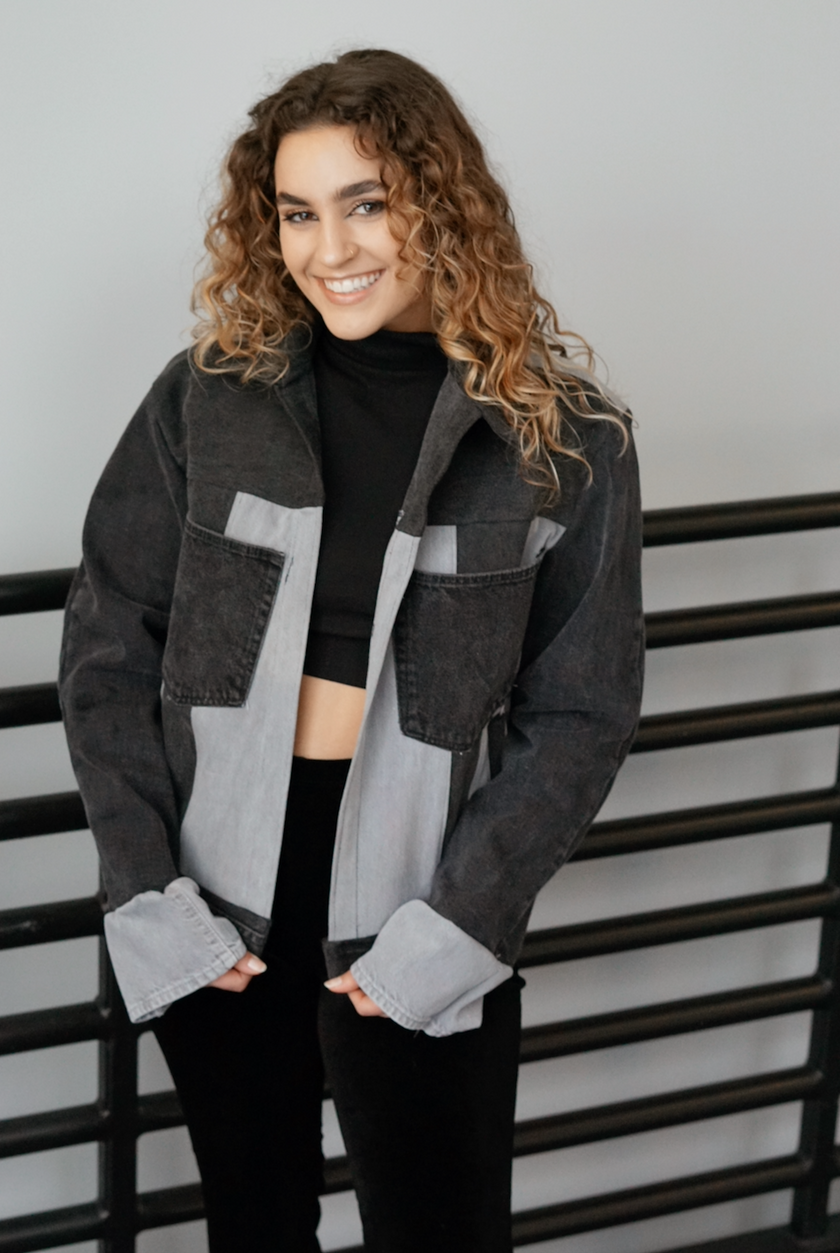 Woman wearing a black color-block denim jacket with contrasting gray denim panels and front patch pockets.