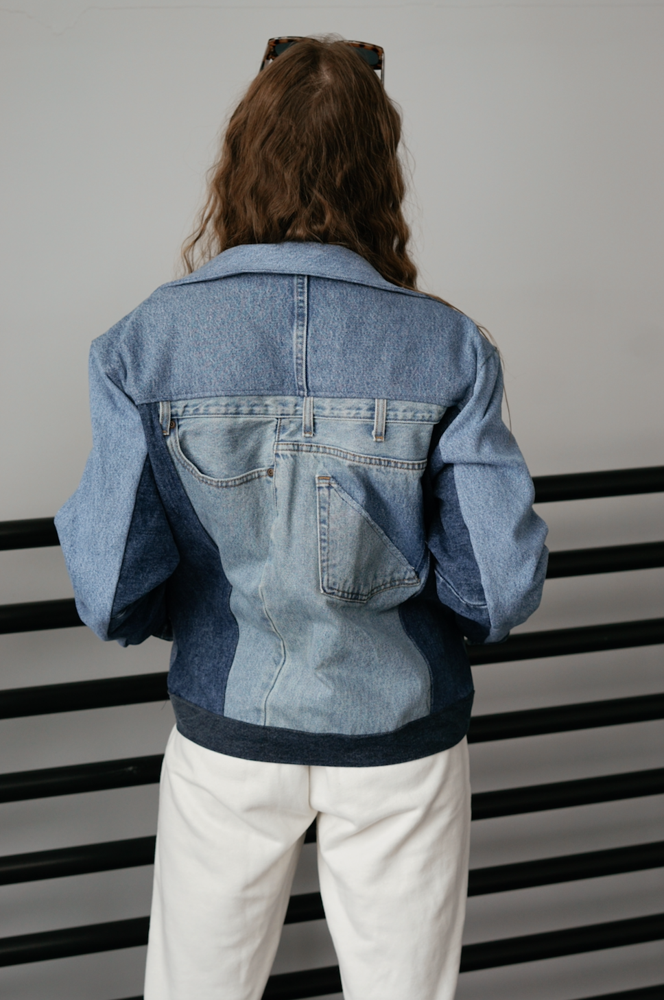 Back view of a woman wearing a light wash color-block denim jacket with oversized fit and contrasting denim panels.