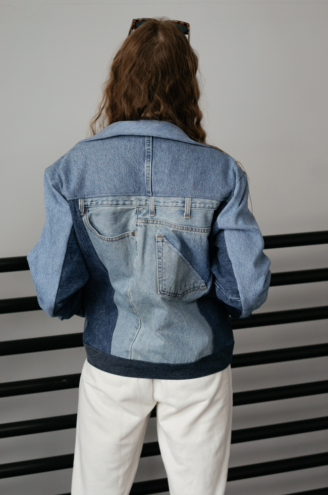 Back view of a woman wearing a light wash color-block denim jacket with oversized fit and contrasting denim panels.