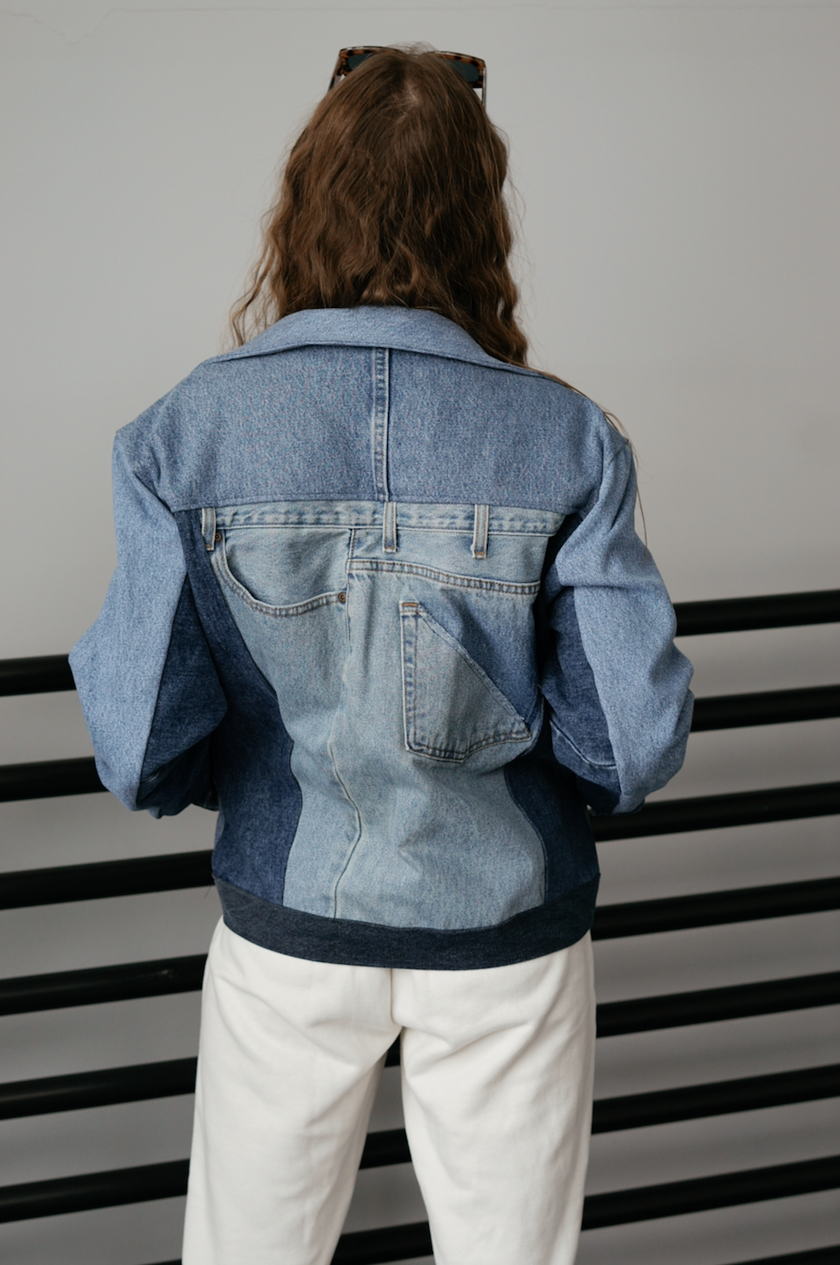 Back view of a woman wearing a light wash color-block denim jacket with oversized fit and contrasting denim panels.