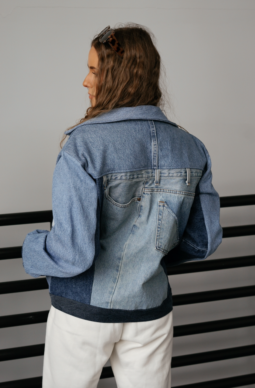 Back angled view of a woman wearing a light wash color-block denim jacket with oversized fit.